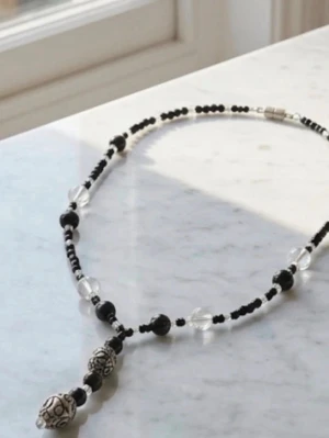 Svart och silverfärgat pärlhalsband - Unikt halsband med svarta och genomskinliga pärlor samt två stora, dekorativa silverfärgade pärlor med snirkligt mönster. Halsbandet har en cool kontrast mellan de mörka och ljusa pärlorna och passar perfekt för dig som gillar detaljer och statement-smycken.