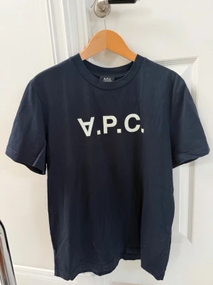 Mörkblå A.P.C. t-shirt - Snygg mörkblå t-shirt från A.P.C. med vit logga tryckt framtill. Klassisk rund hals och korta ärmar. Tillverkad i mjuk bomull för en skön känsla och enkel stil. Kvitto finns!