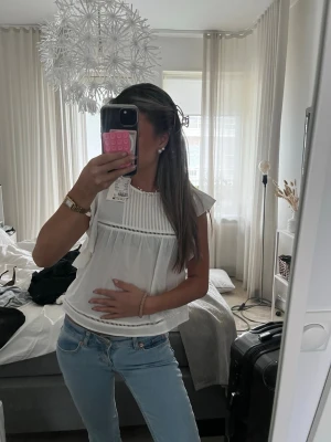 Vit blus med volangdetaljer - Söt vit blus med volangdetaljer på axlarna och dekorativa hålband. Blusen är helt ny från hm med prislapp kvar i storlek XS perfekt till vardags🥰