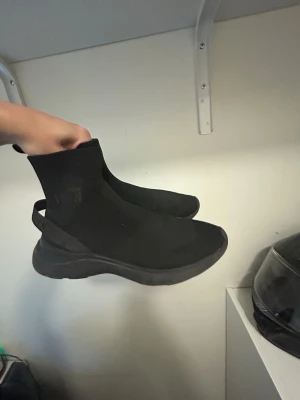 Svarta dsquard sock-sneakers med tjock sula - Säljer ett par helsvarta dsquard sock-sneakers med stretchig stickad ovandel och chunky sula. Skorna har en modern siluett med högt skaft och en praktisk hälflik för enkel påtagning. Perfekta för dig som gillar minimalistisk och sportig stil.