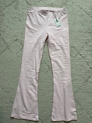 Ljusrosa utsvängda leggings - Säljer ett par ljusrosa leggings med utsvängda ben och normal midja. De har en mjuk och stretchig känsla, perfekta för en trendig och bekväm look. Materialet ser ut att vara bomullsblandning. Elastisk midja för extra komfort.