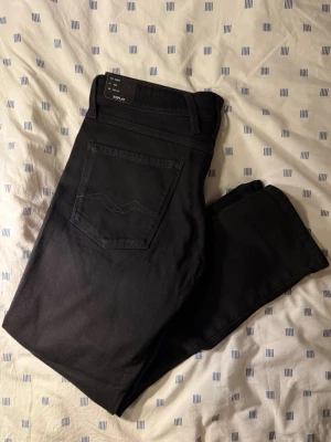 Svarta slim jeans från Replay - Snygga svarta slim fit jeans från Replay, modell Anbass. Jeansen har klassisk femficksdesign och raka ben. Materialet är mjukt och stretchigt för extra komfort. Perfekta för dig som gillar en modern och stilren look. Storlek w33 L30, helt nya, aldrig använda.