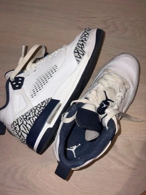 Vita och marinblå Air Jordan sneakers 39 - Snygga vita och marinblå Air Jordan sneakers med ikoniskt elefantmönster på hälen och sulan. Skorna har meshdetaljer på sidorna, klassisk Jumpman-logga på plösen och tålig gummisula. Perfekta för dig som gillar streetwear och sportig stil.
