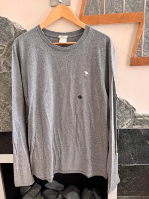 Grå långärmad topp Abercrombie XL - Snygg grå långärmad topp från Abercrombie & Fitch i mjuk bomull. Klassisk rund halsringning och diskret logga broderad på bröstet. 