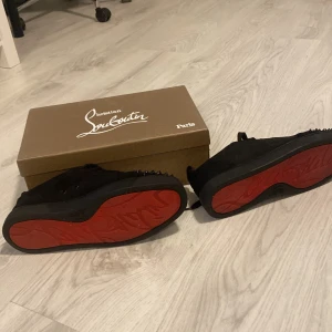 loubs som jag ej har används eftersom dom var för stora. - Svarta sneakers från Christian Louboutin med ikoniska röda sulor och svarta nitar på tån. Skorna har snörning och är tillverkade i mocka för en lyxig känsla. Perfekta för dig som vill sticka ut med en edgy och exklusiv look.