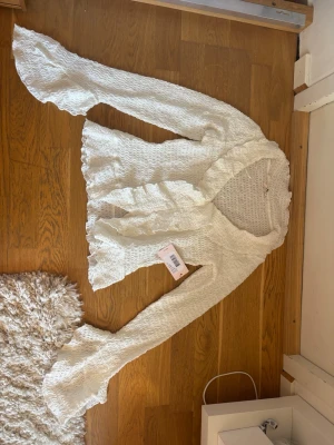 Vit volangblus från Nelly XS - Säljer en superfin vit blus från Nelly i storlek XS. Blusen har långärmad design, volangdetaljer och är gjord i ett vågigt, transparent tyg som ger en luftig och trendig look. Perfekt att styla med jeans eller kjol för en chic outfit.