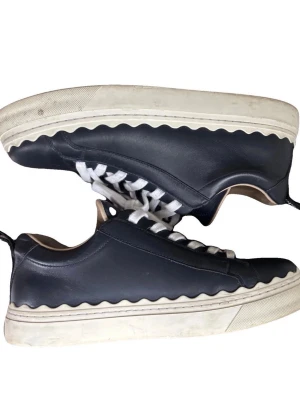 Chloé sneakers - Snygga mörkblå sneakers från Chloé med unik vågig vit sula och vita skosnören. Skorna är tillverkade i slätt läder och har beige insida för extra komfort. Perfekta för dig som vill ha en stilren men ändå lekfull look.