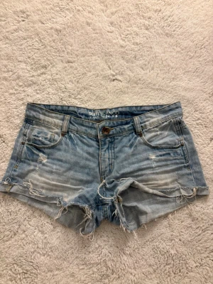 Ljusblå jeansshorts med slitningar - Snygga ljusblå jeansshorts från Suiteblanco med slitna detaljer och fransig kant. Klassisk femficksmodell med knapp och dragkedja framtill. Perfekta för varma dagar och en avslappnad stil. LÅG MIDJADE💕Märket säljs inte längre 