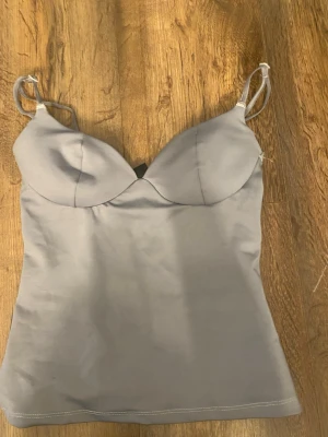 Ljusgrå linnetopp från Gina Tricot - Säljer en ljusgrå linnetopp från Gina Tricot med tunna axelband och formade kupor. Toppen har en slät och mjuk yta, perfekt för att styla med jeans eller kjol. Enkel och stilren design som passar till många olika looks.