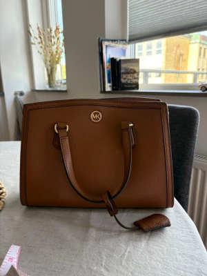 Brun handväska från Michael Kors - Jättebra skick. Kommer med bandet men gjorde ett extra hål på den, se sista bilden. Priset kan diskuteras.