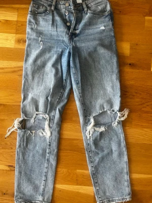Ljusa mom jeans med slitningar - Säljer ett par ljusblå mom jeans med ultra high waist och stora slitningar över knäna. Jeansen har klassisk femficksmodell och är tillverkade i denim. 