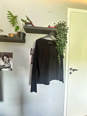 Nudie jeans henley - En enkel svart långärmad topp med rund halsringning och knappar framtill från nudie jeans. Perfekt basplagg som passar till det mesta. Tillverkad i mjukt material för en bekväm känsla.