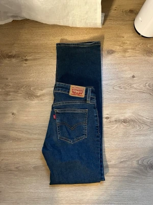 Levi's bootcut jeans i mörkblå denim - Säljer ett par klassiska Levi's jeans i mörkblå denim med bootcut passform. Jeansen har fem fickor, synliga sömmar och en ikonisk läderpatch bak i midjan. Perfekta för dig som gillar tidlös stil och vill ha ett par jeans som alltid funkar. Samma på dom här köp på min vinted 11.ellie.12