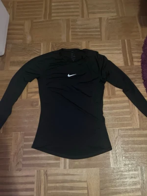 Svart långärmad träningströja Nike - Säljer en svart långärmad träningströja från Nike Pro med Dri-FIT-teknologi. Tröjan har en tight passform och en vit Nike-logga på bröstet. Perfekt för intensiva träningspass eller löpning. Materialet är snabbtorkande och andas bra.
