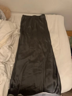 Mörkgrå satinkjol från Gina Tricot - Säljer en lång, mörkgrå satinkjol från Gina Tricot. Kjolen har en glansig finish och en mjuk, följsam passform som ger en snygg siluett. Perfekt att styla med både stickade tröjor och crop tops.