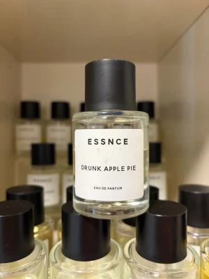 ESSNCE Drunk Apple Pie parfym - Parfymflaska från ESSNCE med doften Drunk Apple Pie. Flaskan är genomskinlig med svart rund kork och vit etikett med svart text. Eau de Parfum med en fräsch och söt äppeldoft, perfekt för dig som gillar unika och fruktiga parfymer.