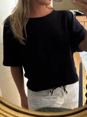 Zara t-shirt med knyt - En marinblå t-shirt i bomull med korta ärmar och rund halsringning, samt knyt längt ner som går att spänna åt. Sparsamt använd! 