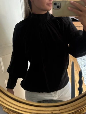 Svart blus med krage - Stilren svart blus med hög krage och rynkade detaljer vid axlar och hals, men knappar baktill. Använd ett fåtal gånger! 