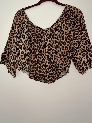 Leopardmönstrad off shoulder blus med knappar - Säljer en luftig blus med leopardmönster och knappar framtill. Blusen är off shoulder och hartrekvartsärmar med lös passform. Materialet känns lätt och flowy, perfekt för en trendig look.