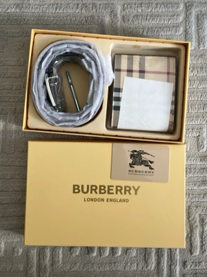 Burberry bälte med plånbok och kort  - Snyggt bälte från Burberry i klassisk beige och brun färgskala med det ikoniska rutmönstret. Kommer i originalförpackning och passar perfekt till att lyfta vilken outfit som helst. Metallspänne i silverfärg ger en stilren touch.