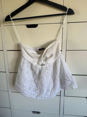 Vit broderad linnetopp från Gina Tricot - Söt vit linnetopp från Gina Tricot i storlek XS. Toppen har tunna axelband, smock upptill och broderade blommor över hela tyget. Perfekt för sommardagar och ger en fräsch och luftig känsla.