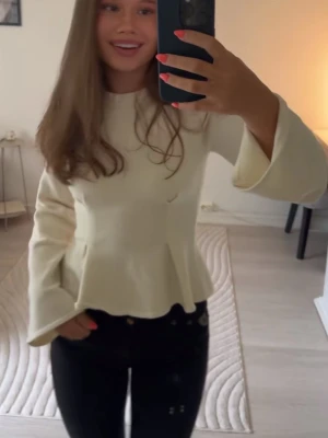 Vit peplum topp med vida ärmar - Snygg vit topp med peplumskärning och vida långärmar. Toppen har en rund halsringning och är perfekt för dig som gillar en feminin och trendig stil. Passar till både jeans och kjol.