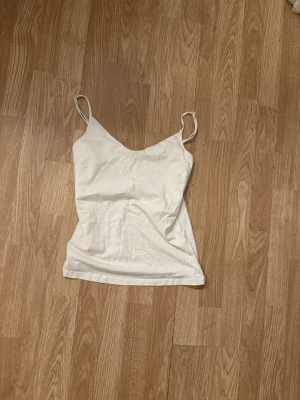 Vit enkel linnetopp - Säljer en vit linnetopp med smala axelband och v-ringad hals. Toppen är ärmlös och har en clean, minimalistisk look som passar perfekt till jeans eller kjol. Materialet känns mjukt och lätt, perfekt för varma dagar.