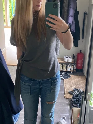 Grå topp med knyt från ZARA - Säljer en stilren grå topp från ZARA med korta ärmar och snygg knytning i sidan. Toppen har en rund halsringning och är gjord i mjukt, ribbat material som ger en skön känsla. Perfekt att matcha med jeans eller kjol för en enkel men trendig look.