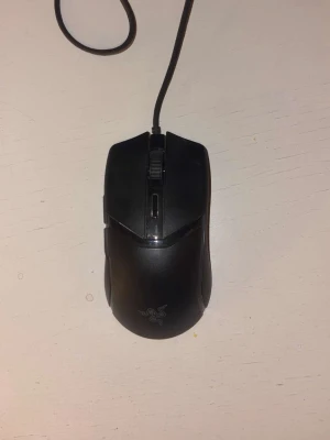 Svart gamingmus från Razer - Säljer en svart gamingmus från Razer med sladd. Musen har en ergonomisk form och är perfekt för gaming eller arbete vid datorn. Klassisk design med Razer-loggan på ovansidan och scrollhjul i mitten. Köptes för inte alls längre sen nytt skick 