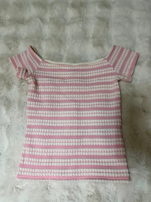 Rosa och vit randig topp från Nelly - Söt topp med rosa och vita ränder i ett stickat material. Modellen är offshoulder med korta ärmar och har en mjuk, bekväm passform. Perfekt för dig som gillar en gullig och avslappnad stil.
