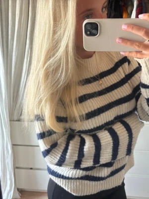 Randig stickad tröja i offwhite och marinblå - Säljer en mysig stickad tröja från h&m i offwhite med marinblå horisontella ränder. Tröjan har en avslappnad passform, rund halsringning och ribbstickade muddar. Perfekt för lager på lager och enkel att styla till både jeans och kjol. 