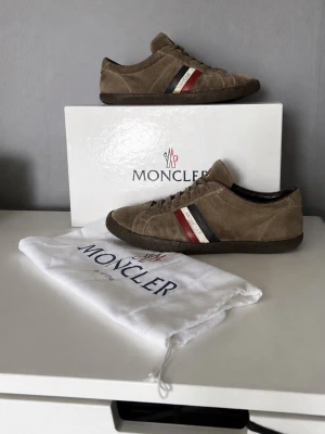 Moncler skor - Säljer ett par bruna Moncler skor i mocka, storlek 42. Skorna är i hyfsat skick. Tecken på användning men kan absolut användas mer. Box och dustbag följer med skorna!🙌