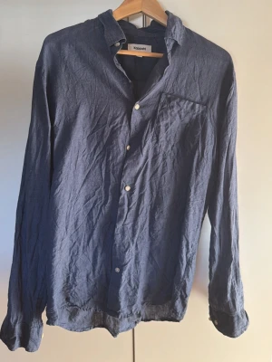 Mörkblå linneskjorta från Kappahl - Snygg mörkblå skjorta från Kappahl i luftig linne. Klassisk modell med lång ärm, bröstficka och vita knappar. Perfekt för dig som gillar en avslappnad men stilren look. Köptes för 550kr