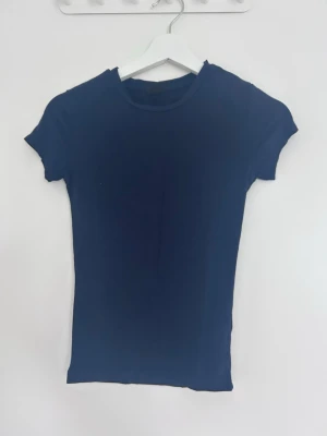 Mörkblå enkel t-shirt - Säljer en mörkblå t-shirt med rund hals och korta ärmar. T-shirten har en klassisk passform och är tillverkad i mjukt bomullsmaterial. Perfekt basplagg till garderoben.
