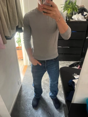Crew Neck Merinoull Tröja - En rikigt kvalité och stilren ljusgrå tröja med rund halsringning och långa ärmar. Tröjan har ribbade muddar vid ärmslut och nederkant. Perfekt att matcha med jeans nu till hösten. Mycket bra skick på plagget i sig, använd endast ett fåtal gånger. Minimalt slitage i ena armhålan men påverkar varken looken eller användningen. Pris går att diskuteras! 