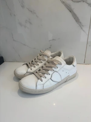 Vita phillipe modell skor - Stilrena vita sneakers från Philippe Model i läder med beigea skosnören och diskreta detaljer på sidan. Klassisk låg modell med rund tå och vadderad häl för extra komfort. Passar perfekt till jeans eller shorts för en clean look. Du får även med box och dustbag