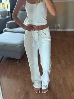 Vita raka jeans - Säljer ett par vita jeans med rak passform och låg midja. Jeansen har klassiska fem fickor, bälteshällor och knappgylf. Materialet är denim i bomull och de har en stilren look som passar till det mesta.