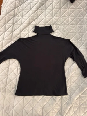 Svart cold shoulder polotopp med 3/4 ärm - Säljer en svart polotopp med 3/4 ärm och hög krage. Toppen har en soft touch loose passform och är tillverkad i ett mjukt, stretchigt material som känns skönt mot huden. Perfekt att styla med jeans eller kjol för en clean look. Endast andvänd en gång!!