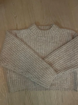 Beige grovstickad tröja - Säljer en beige grovstickad tröja med rund hals och långa ärmar. Tröjan har en avslappnad passform och ribbstickade muddar vid ärmslut, hals och nederkant. Perfekt för kyliga dagar och enkel att matcha med jeans eller kjol.