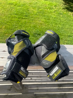 Armbågsskydd Bauer Mach - Säljer ett par svarta och gula armbågsskydd från Bauer Supreme Mach-serien. Storlek Senior Sr Medium M. Fungerar utan anmärkning.