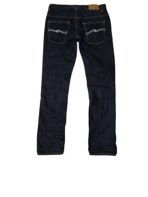 Blåa Nudie Jeans - Snygga mörkblå nudie jeans med raka ben och kontrastsömmar. Bakfickorna har en vågig detalj i vitt och orange, vilket ger en unik look. Jeansen har klassisk femficksmodell och är tillverkade i denim. Perfekta för dig som gillar stilrena men ändå personliga jeans. I storleksskalan XS-XL sitter denna som S/M.