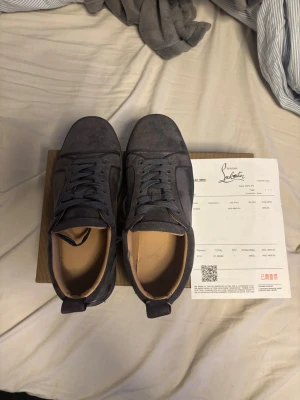 Christian Louboutin grå mockasneakers - Grå sneakers i mocka från Christian Louboutin med klassisk röd sula och diskret logga. Lågt skaft, rundad tå och snörning framtill. Insidan är ljusbeige och sulan har den ikoniska röda färgen med signatur. Perfekt för dig som gillar lyxiga och unika sneakers. Lite smutsigare på undersidan än på bilden . Sitter ganska smått i storleken 