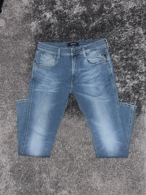 Ljusblå raka jeans med slitningar från Replay - Säljer ett par ljusblå jeans med raka ben och diskreta slitningar från Replay. Jeansen har klassisk femficksdesign, bälteshällor och en snygg tvättad look. Perfekta för en avslappnad och trendig stil.