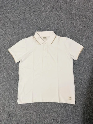 Vit pikétröja från Pull&Bear - Klassisk vit pikétröja från Pull&Bear med korta ärmar och beige detalj på kragen. Hör av dig vid funderingar eller behov av fler bilder!🤗🤗