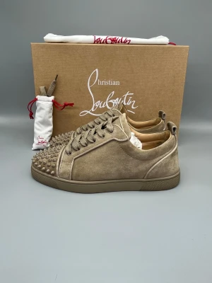 Christian Louboutin Louis Junior Spikes Orlato Sneaker Beige | 40 - Begagnade sneakers i mycket gott skick, beige färg. Box, dustbag och nya snören ingår.