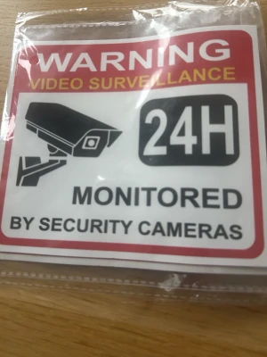 Varningsskylt videoövervakning 24H / 2styck - Skylt med texten 'Warning Video Surveillance 24H Monitored by Security Cameras'. Röd, vit och svart färg, fyrkantig form och tillverkad i plast. Perfekt för att tydligt visa att området är övervakat dygnet runt.