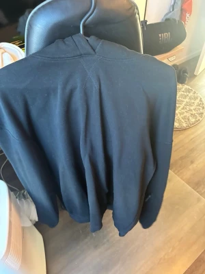 Svart hoodie med luva - En enkel och stilren svart hoodie med luva och långa ärmar. Hoodien har diskreta sömdetaljer och ser riktigt chill ut. Perfekt för dig som gillar en clean look och vill ha något bekvämt att slänga på sig. Materialet ser ut att vara mjukt och skönt.