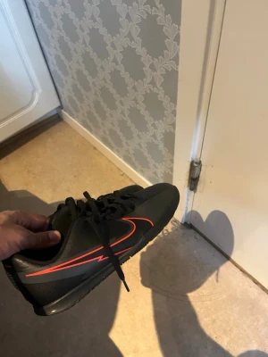 Svarta sneakers med röd detalj - Snygga svarta sneakers med en röd sicksack-detalj på sidan och svarta skosnören. Skorna har en låg profil och en sportig look, samt röd insida. Materialet ser ut att vara syntet med gummisula. Perfekta för dig som gillar stilrena men ändå iögonfallande skor.