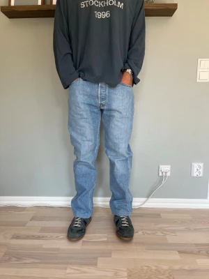 Levi’s 501 Vintage Jeans W32 L32 Ljusblå Denim - Levi’s 501 i klassisk ljusblå tvätt med naturligt slitage och fin patina. Rak passform genom hela benet, knappgylf, klassisk femficksmodell med skinnlapp bak.  Skick: bra skick, inga hål eller fläckar Material: denim (100% bomull) Midja: W32 Innerbenslängd: L32 Modell: 175 cm / 65 kg — bär vanligtvis W30/32, sitter avslappnat/relaxed på bild