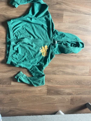 Grön zip up hoodie med Seattle-tryck - Snygg grön hoodie med dragkedja och huva. På bröstet finns ett gult och vitt tryck med texten 'Seattle' och detaljer som WA EST. 93. Hoodien har ribbade muddar och är perfekt för en chill och sportig look.